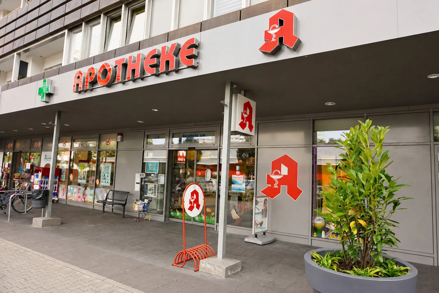 Die Schaufensterfront der Apotheke von der Seite, mit Fahrradständer und Sitzbank